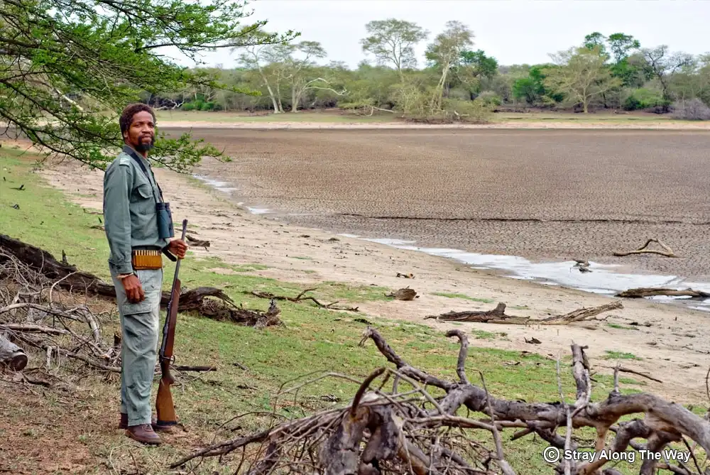 A game ranger standing with a rifle next to a dry pan in the Ndumo Game Reserve.